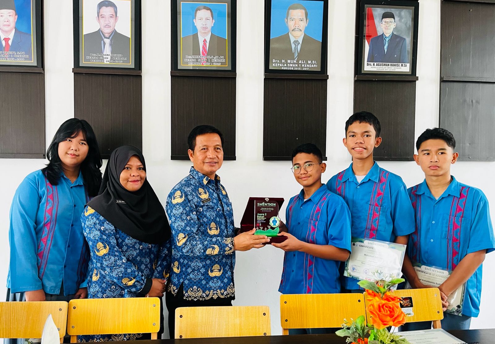 Kepala SMAN 1 Kendari, Ruslan (tengah), saat menerima plakat penghargaan dari Tim SMAN 1 Kendari usai meraih Juara 2 Lomba Debat Bahasa Indonesia pada ajang Smention 2026 tingkat nasional. (FOTO: FAYSAL/MS)